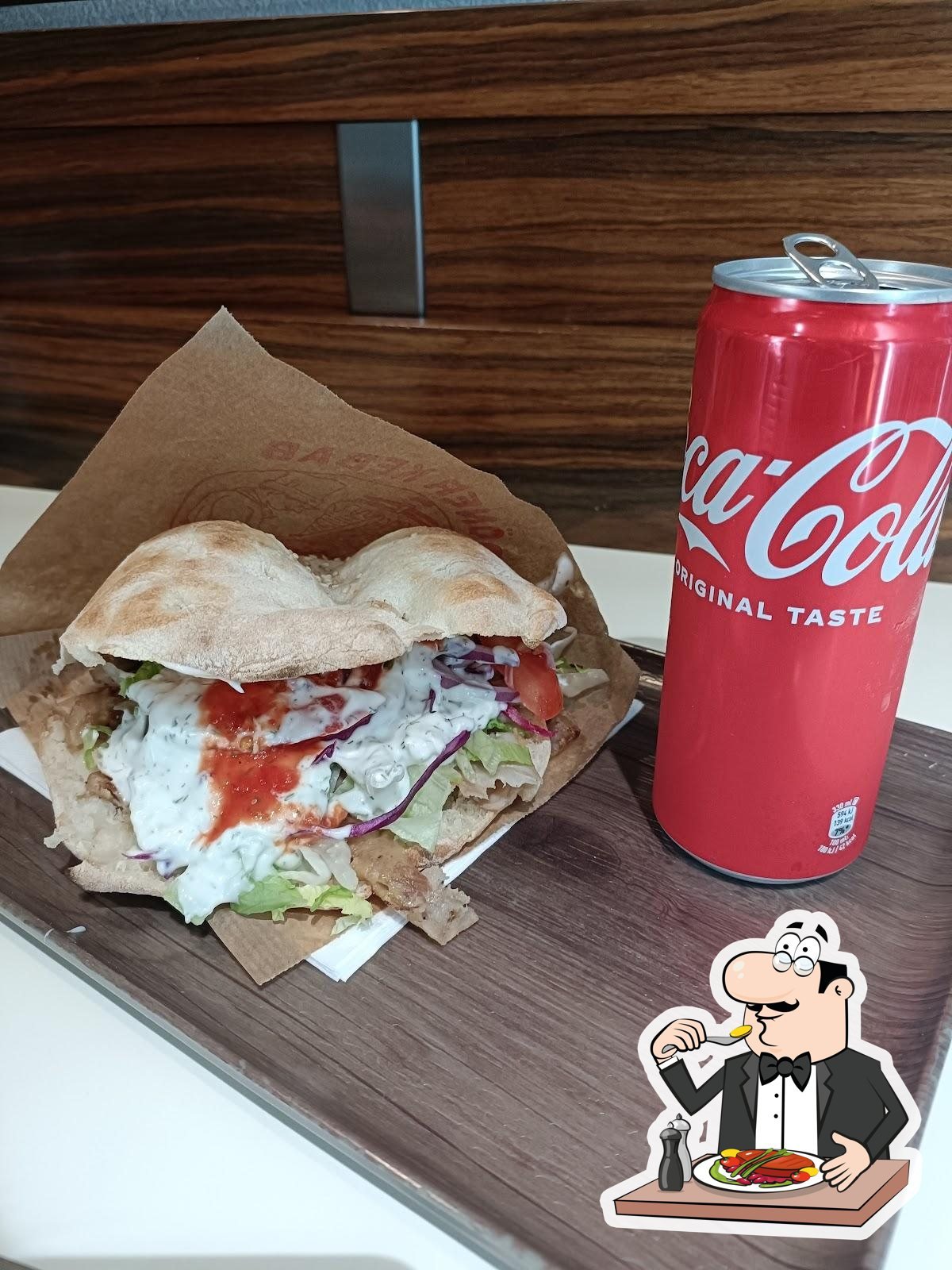 Panino doner kebab con carne allo spiedo, insalata, cavolo rosso, pomodoro e salse bianca e rossa accanto a una lattina di Coca-Cola