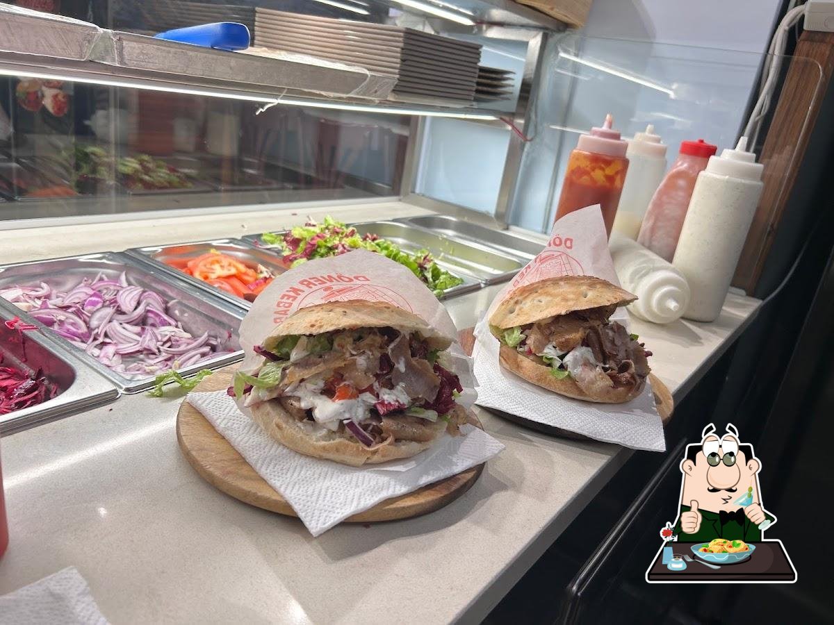 Due panini con carne e salsa bianca nella carta «Döner Kebab» su taglieri di legno, vicino a cipolla rossa e insalata
